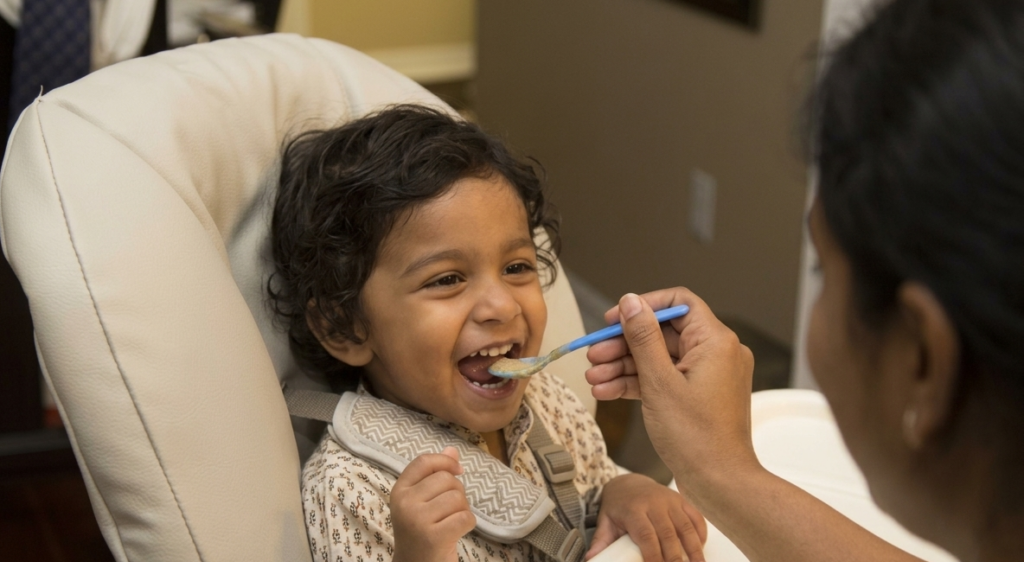 A parent sitting calmly with a toddler at a shared table and feeding them. How to stop force feeding your toddler and trust her own regulation at Blue Blocks Montessori School, Hyderabad.