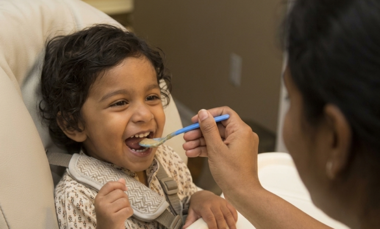A parent sitting calmly with a toddler at a shared table and feeding them. How to stop force feeding your toddler and trust her own regulation at Blue Blocks Montessori School, Hyderabad.