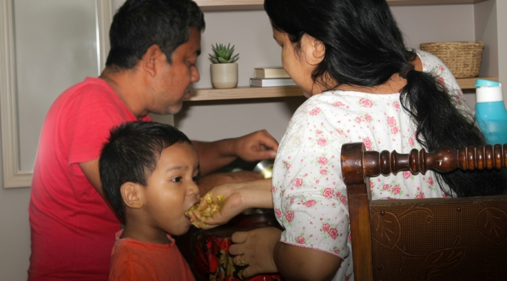 Parents sitting with their toddler at a shared table, feeding them. How to stop force feeding your toddler and trust her own regulation at Blue Blocks Montessori School, Hyderabad.